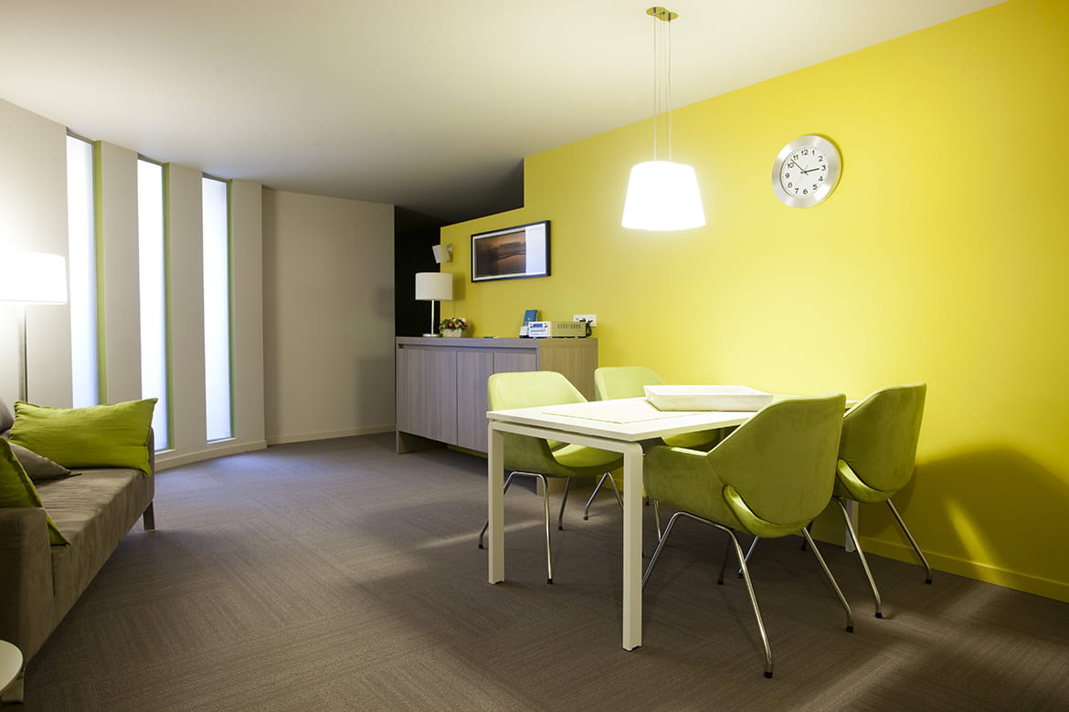 Ontvangstruimte met zachtgele muur, tafel, stoelen en grijze zetel